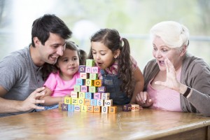 Cute girl blowing alphabet blocks while family looking at it in house