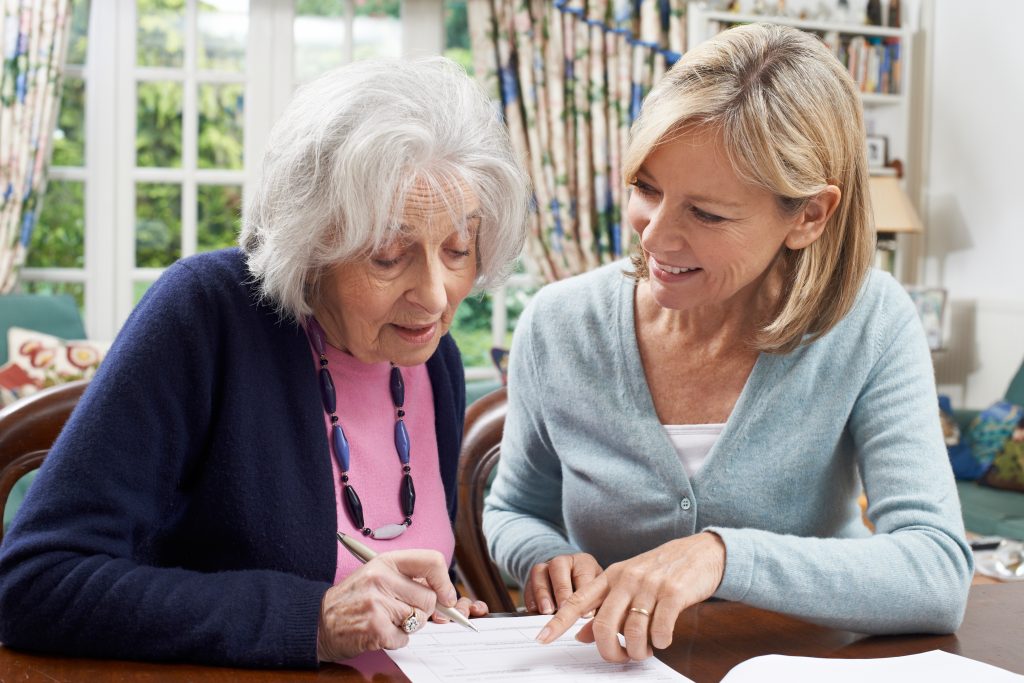 middle aged blonde woman helps elderly woman fill out paperwork