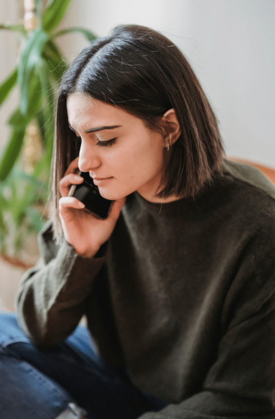Woman with straight dark hair in dark sweater listens to someone on the phone.